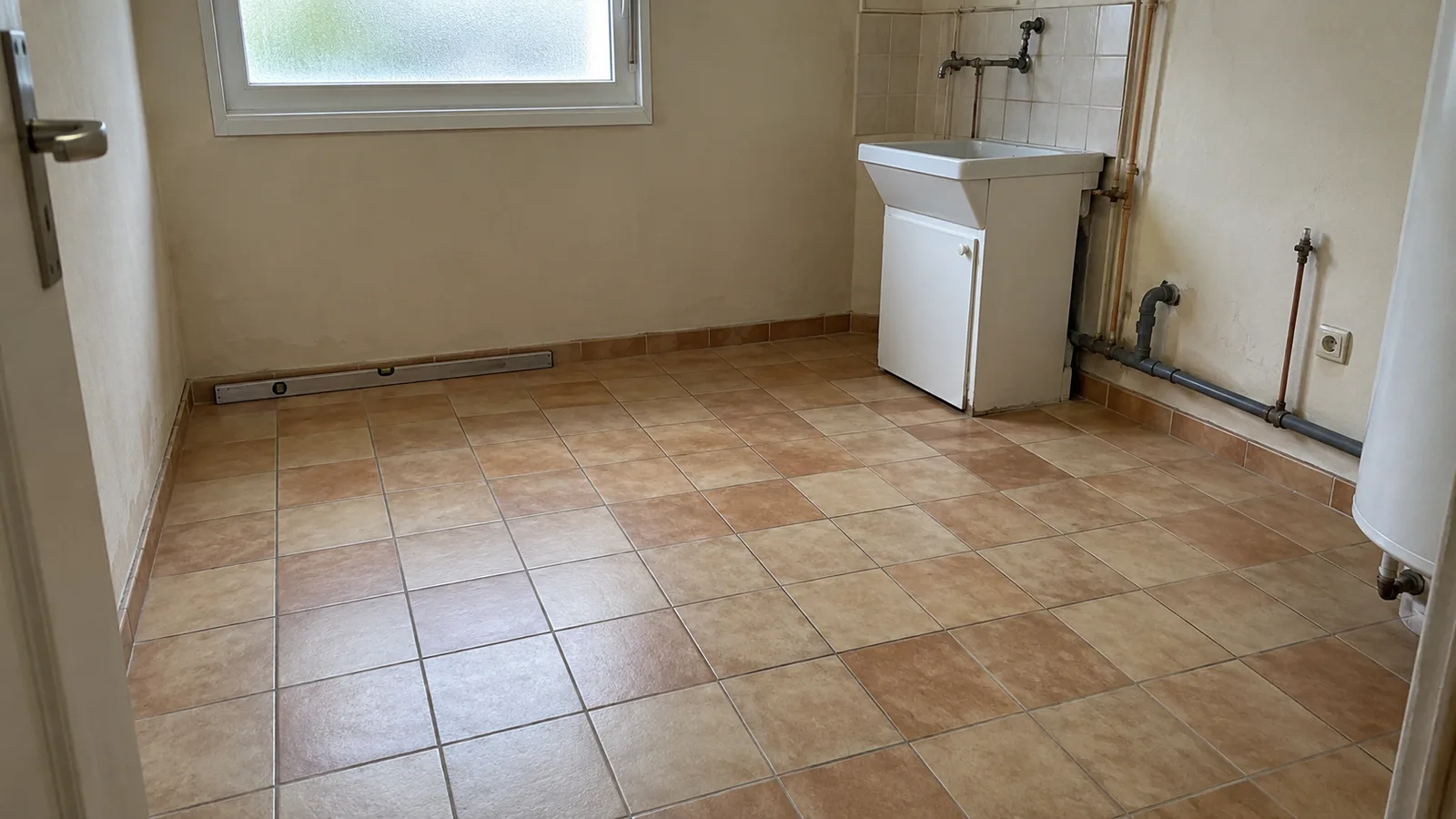 Ancien carrelage beige dans une buanderie en rénovation avant la pose d’un sol résine